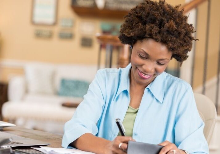 Black woman smiling while writing in checkbook